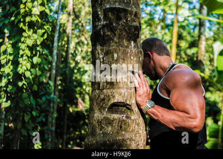 Nessun volto. irriconoscibile persona dell'uomo appoggiato sul tronco di albero mentre cercando nella foresta. mano sul tronco. La carica di energia del legno. atleta maschio con forte Foto Stock