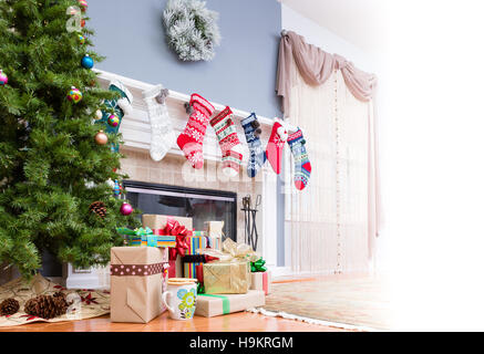 Pila di regali di Natale sotto l'albero con calze colorate appeso sul mantelpiece e un alto tasto luminoso spazio copia al lato per le vostre vacanze Foto Stock