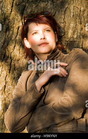 Ritratto di un giovane, i capelli rossi donna appoggiata ad un tronco di albero Foto Stock