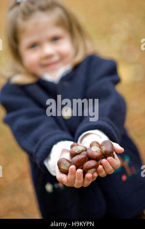 7-year-old girl, in autunno, tenendo le castagne Foto Stock