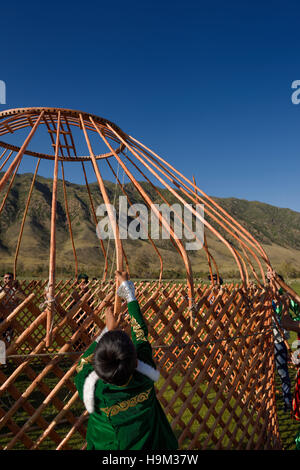 Ragazzo giovane contribuendo ad assemblare il telaio in legno di un Yurt soggiornare in Kazakistan Foto Stock