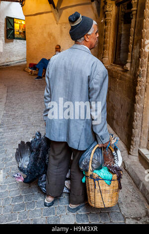 Un uomo locale passeggiate per le strade della Medina con una borsa da shopping e vivere il pollo, Fez el Bali, Fez, in Marocco Foto Stock