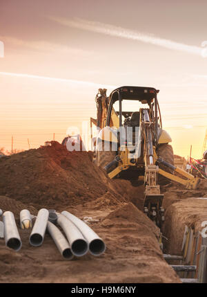 Bulldozer carving foro per posa di tubo sul sito di costruzioni. Fine della giornata di lavoro del tramonto. Foto Stock