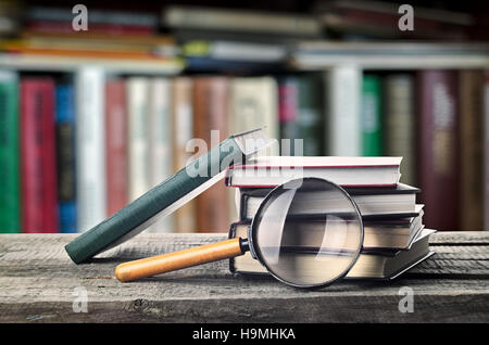 Pila di libri e alla lente di ingrandimento su un tavolo di legno con scaffale, invito a studiare letterature, vicino, sala lettura Foto Stock