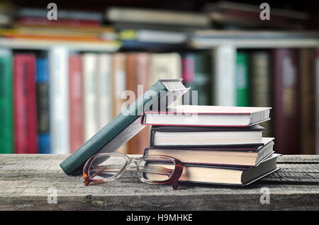 Pila di libri e i bicchieri sul tavolo di legno con scaffale, invito a studiare letterature, vicino, sala lettura Foto Stock