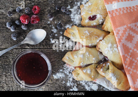 La cottura con marmellata di frutti di bosco su una tavola di legno in stile rustico decorata con frutti di bosco surgelati. Vista dall'alto. In stile vintage. Luce naturale. In casa la cottura. Foto Stock