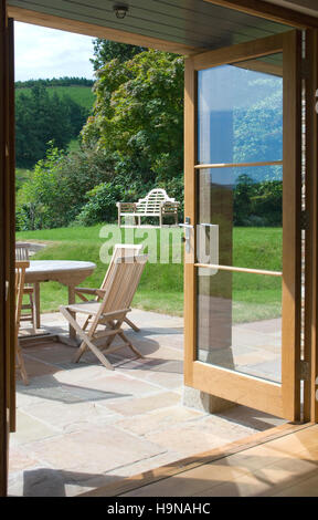 Finestre francesi che si aprono su di un patio e un giardino con tavolo e sedie. Foto Stock