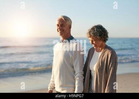 Colpo all'aperto di felice coppia matura camminando lungo la spiaggia. Senior uomo e donna senior facendo una passeggiata sulla riva del mare. Foto Stock