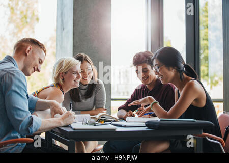 Contenti i giovani studenti universitari che studiano con libri in biblioteca. Un gruppo di persone e multirazziale in college library. Foto Stock