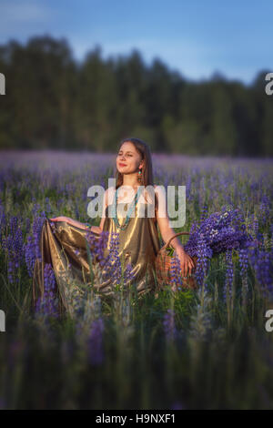 Bellissima ragazza con un cesto di fiori in un campo di lupino. Foto Stock