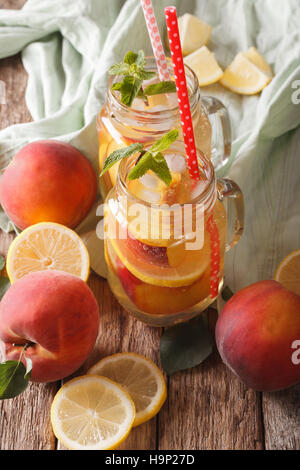 Bevanda rinfrescante con limone, pesca, ghiaccio e menta in un vasetto di vetro closeup sul piano verticale. Foto Stock