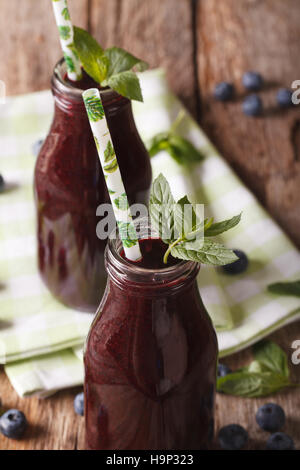 Fresco e salutare mirtillo succo in una bottiglia di vetro su una tabella macro verticale. Foto Stock