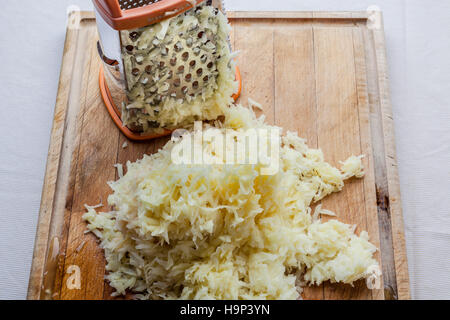 Patate grattugiate con metallo grattugia permanente sul tagliere di legno dal di sopra Foto Stock