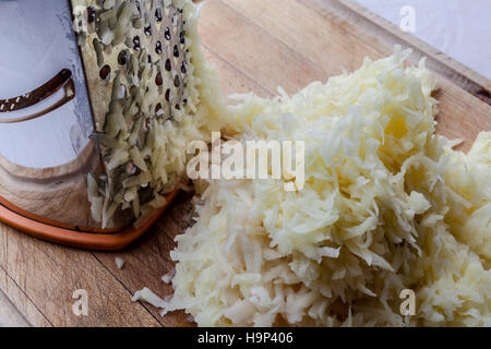 Patate grattugiate con metallo grattugia permanente sul tagliere di legno da elevato angolo closeup Foto Stock