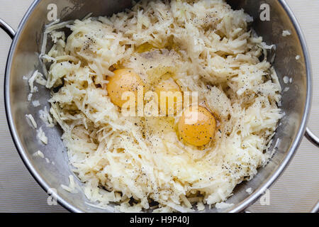 Patate grattugiate e tre uova con il condimento per latkes nel recipiente di metallo da sopra Foto Stock