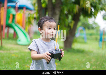 Little Asian kid tenendo un telecomando radio (controllo microtelefono per elicottero , fuco o piano presso il parco giochi, scuola cantiere. Capretto felice in kin Foto Stock