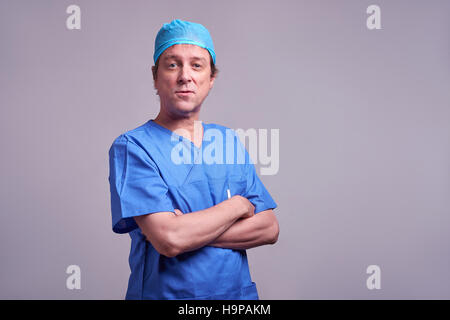 Una mezza età medico maschio con fiducia permanente in uno scrub blu Foto Stock