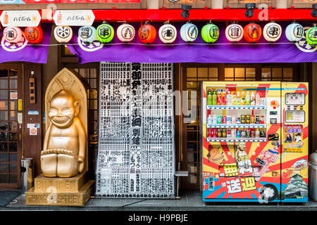 Giappone, Osaka, Shinsekai. Billiken popolare statua fuori del ristorante yokozuna, vendita Kushi-katsu, un famoso Osaka specialità alimentari. Distributore automatico. Foto Stock