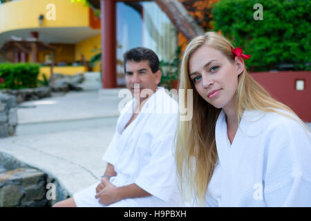 Close up ritratto di giovane donna, con l'uomo in background, indossando accappatoi bianchi all'aperto Foto Stock