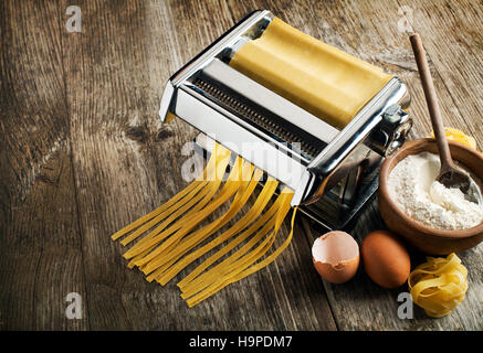 Pasta fresca facendo in macchina su sfondo di legno Foto Stock