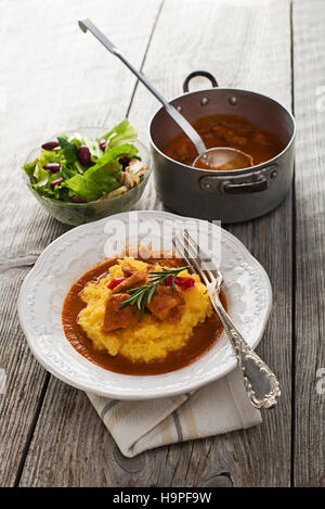 La carne servita sulla polenta su una piastra bianca con insalata Foto Stock