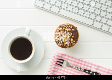 Pausa per il caffè e muffin presso l'ufficio. Concetto con caffè e muffin alla tastiera del computer. Foto Stock