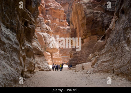 I turisti a piedi attraverso il Siq, passato antico muro incisioni, verso l'ingresso di Petra, Giordania Foto Stock
