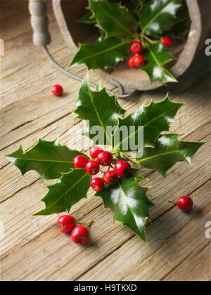 Holly foglie (ilex), decorazione di Natale con bacche rosse su legno Foto Stock