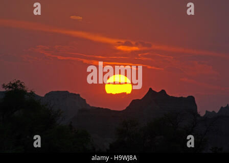 Questa immagine mostra un tramonto sul Badlands National Park. I colori vivaci del sole che tramonta illuminano le caratteristiche formazioni geologiche del parco, offrendo una vista mozzafiato del paesaggio unico del parco al crepuscolo. Foto Stock
