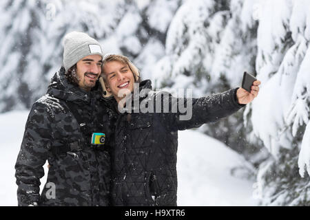 Giovane uomo giovane tenendo Selfie foto nella foresta di neve Outdoor ragazzi tenendo le mani Foto Stock