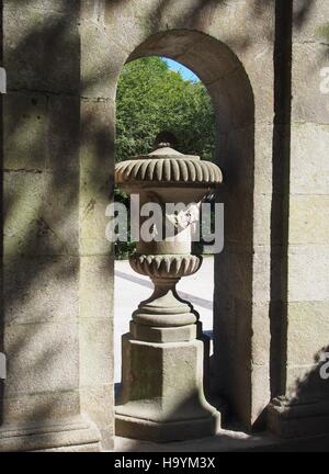 Stile classico vaso di pietra nel Parco Alameda, Santiago de Compostela, Galizia, Spagna, impostato in un arco in pietra e ombreggiata da fogliame Foto Stock