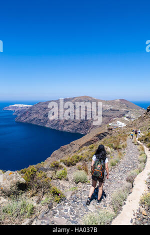 Giovane ragazza camminare lungo il bordo del vulcano da Fira a Oia sull'isola greca di Santorini su un luminoso giorno caldo e soleggiato Foto Stock