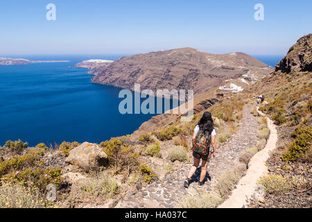 Giovane ragazza camminare lungo il bordo del vulcano da Fira a Oia sull'isola greca di Santorini su un luminoso giorno caldo e soleggiato Foto Stock