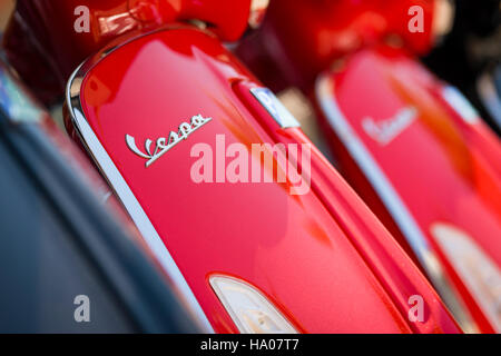 Close-up di Vespa logo a un colore rosso brillante Vespa scooter parcheggiate fuori su una strada al sole Foto Stock