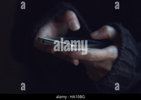 Vista frontale ravvicinata di una donna in maglione scuro mani tenendo un telefono e digitando Foto Stock