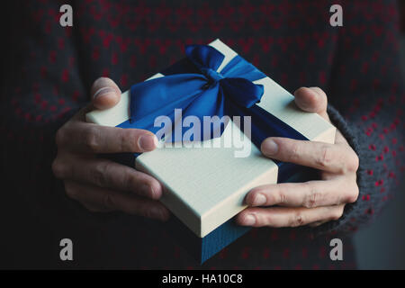 Vista frontale in prossimità di un uomo con un maglione nero tenendo un regalo con nastro blu Foto Stock