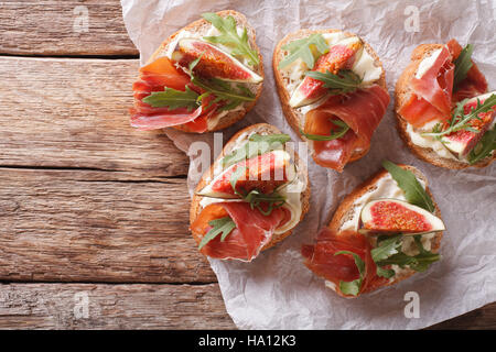 Bruschetta con fichi, prosciutto, rucola e crema di formaggio vicino sul tavolo. vista orizzontale dal di sopra Foto Stock