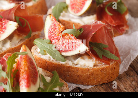 Bruschetta con fichi, prosciutto, rucola e crema di formaggio macro sul tavolo. orizzontale. Stile rustico Foto Stock