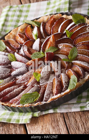 Pane appena sfornato prugna tart decorate con la menta e lo zucchero in polvere di close-up sul tavolo. In verticale Foto Stock