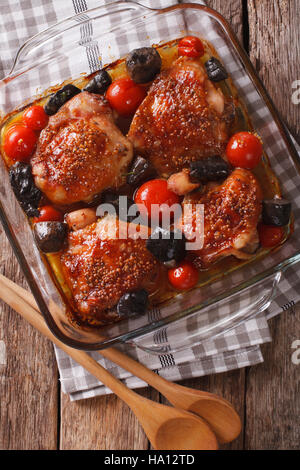 Cotto coscia di pollo con senape e pomodori e funghi selvatici da vicino in una teglia sul tavolo. vista verticale da sopra Foto Stock