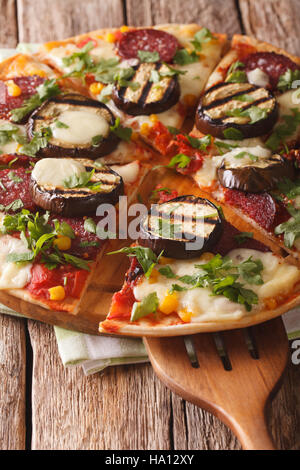 Pizza con le melanzane, salame, mais e mozzarella close up su una tavola di legno verticale. Foto Stock