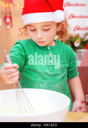 Ritratto di un grazioso piccolo ragazzo indossa red Santa hat rendendo biscotti di Natale a casa felice tempo di festa, preparazione per vacanze invernali Foto Stock