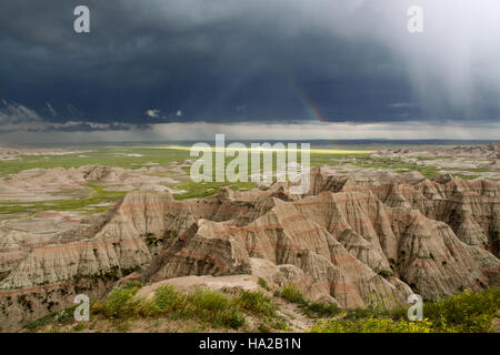 L'immagine cattura un arcobaleno che si forma durante una tempesta nel Badlands National Park, un paesaggio naturale unico nel South Dakota. Conosciuto per le sue impressionanti formazioni geologiche, il parco offre condizioni meteorologiche drammatiche che creano scene pittoresche. Foto Stock