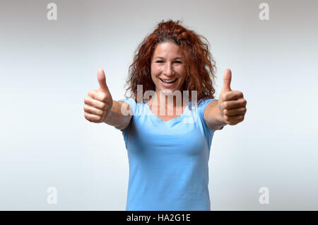 Entusiastico motivati attraente giovane donna dando un pollice in alto gesto di approvazione e di successo con un sorriso raggiante Foto Stock