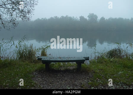 Un banco sulla sponda di un fiume nella nebbia Foto Stock