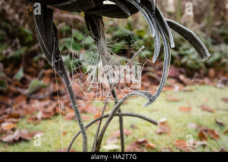 Autunnale coperto di brina ragnatela sulla statua di metallo con caduto foglie marroni sull'erba in background Foto Stock