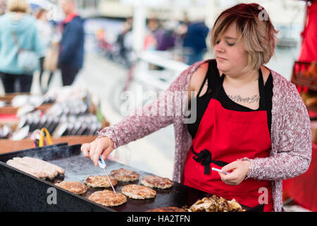 La sicurezza alimentare del Regno Unito: una donna verificando che gli hamburger cottura su una strada di stallo alimentari hanno raggiunto la temperatura sicura utilizzando un digital hand-held termometro Foto Stock