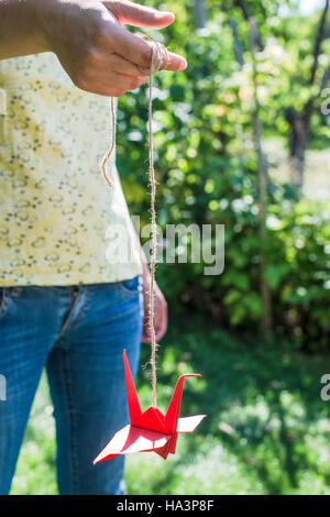 Donna tenere red origami gru in giardino Foto Stock