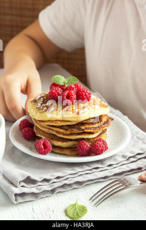 Bambino mangiare sano Colazione a casa - frittelle con lamponi sulla piastra con i bambini le mani Foto Stock