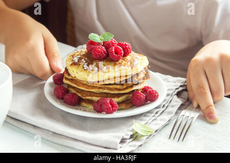 Bambino mangiare sano Colazione a casa - frittelle con lamponi sulla piastra con i bambini le mani Foto Stock